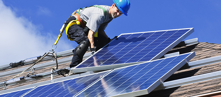 Guy installing solar panels on the top of the roof during a sunny day